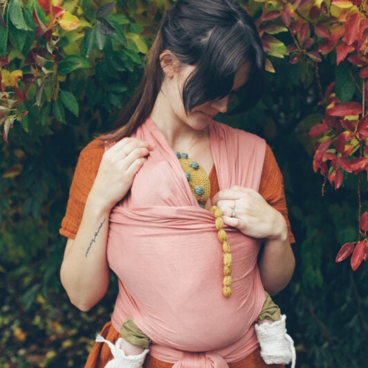 young mother outdoors carrying new baby in a wrap